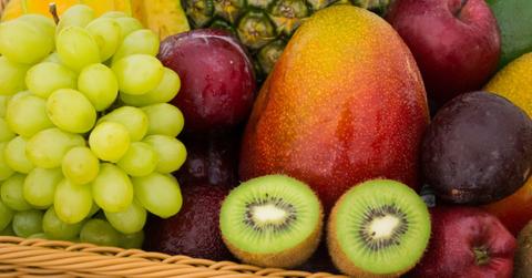 A closeup of a basket of fruit that includes plums, kiwi, mango, and grapes