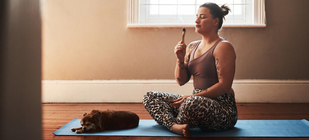 A person burning incense on a yoga mat with a dog.
