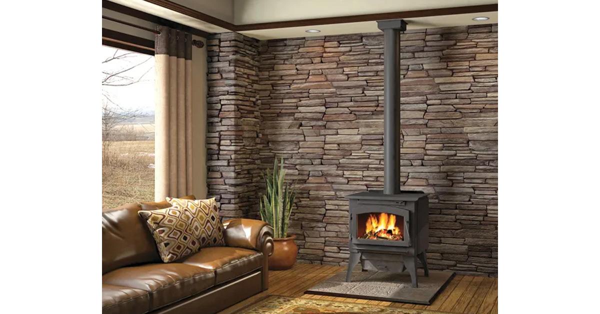 wood stove with fire inside in a room with wood floors, stone walls, and a leather sofa.