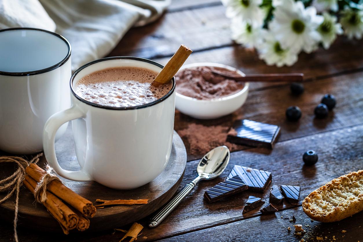 A cinnamon stick is inside a cup of coffee beside blueberries, chocolate, and more cinnamon sticks.