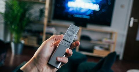 A person holds a silver remote control while turning on the TV