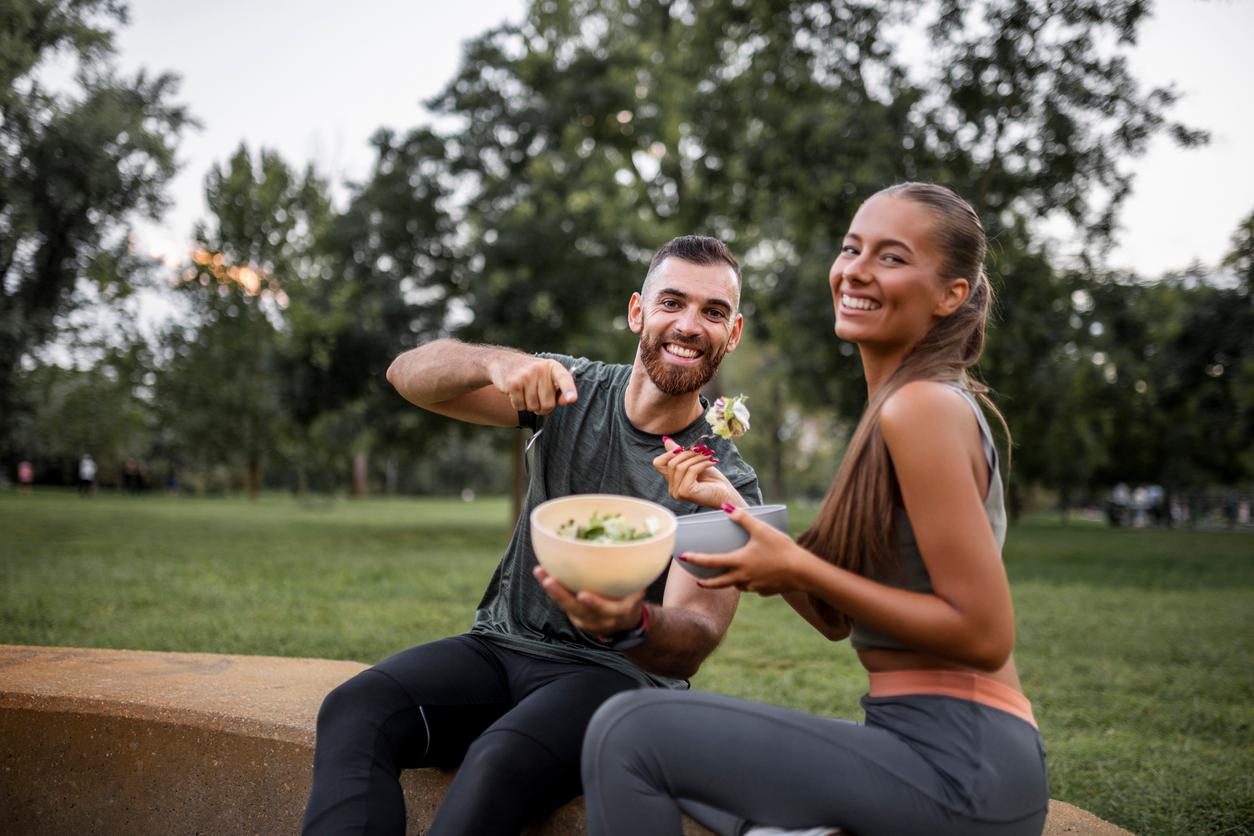 Two vegan athletes share a meal together in a park after exercising outdoors.