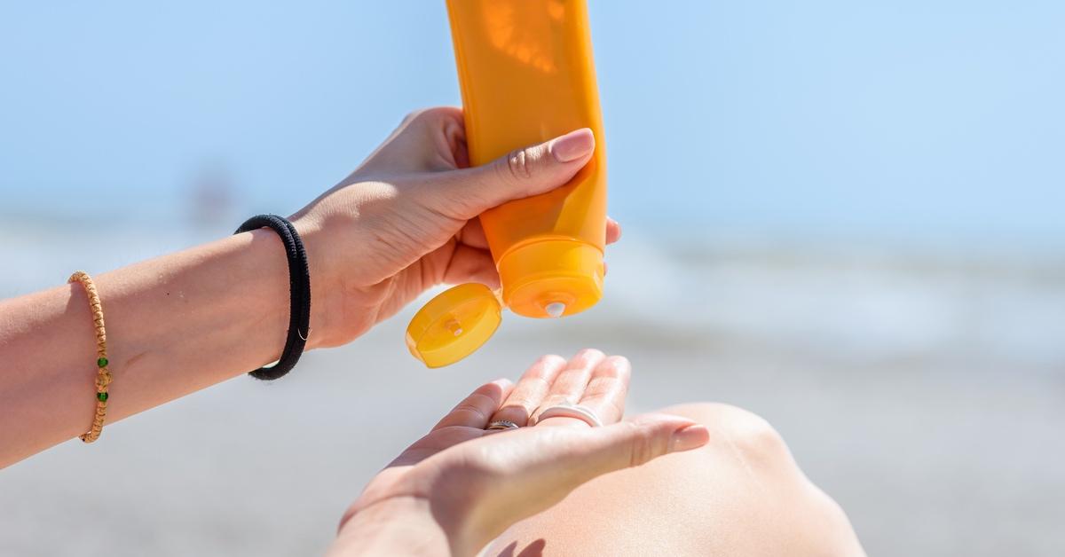 Person pouring sunscreen from an orange bottle into their hand.