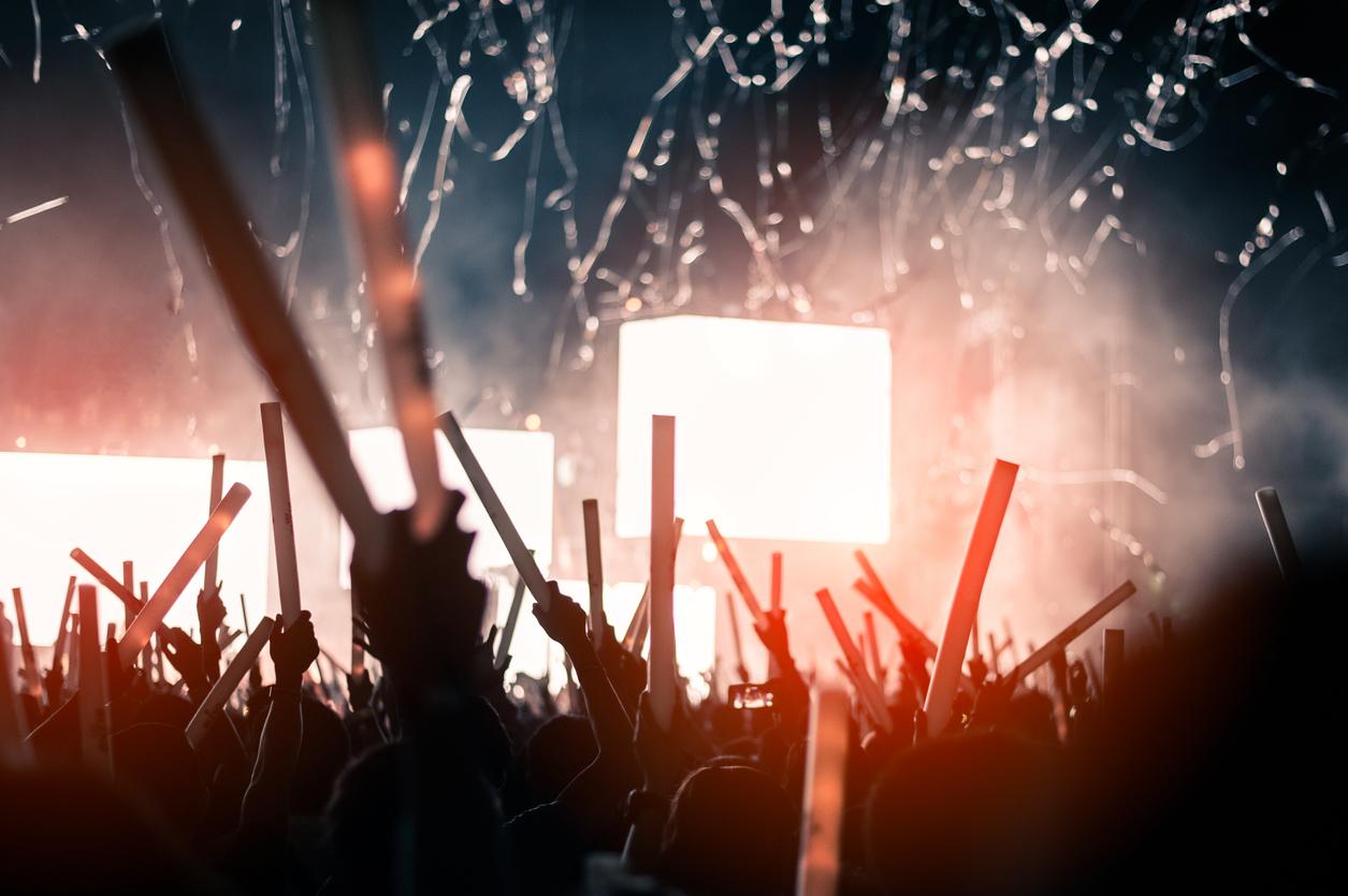 Crowd members at a music festival hold glow sticks as confetti shoots into the air.