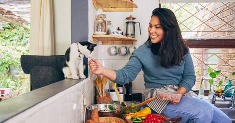 A woman feeds her cat in the kitchen.