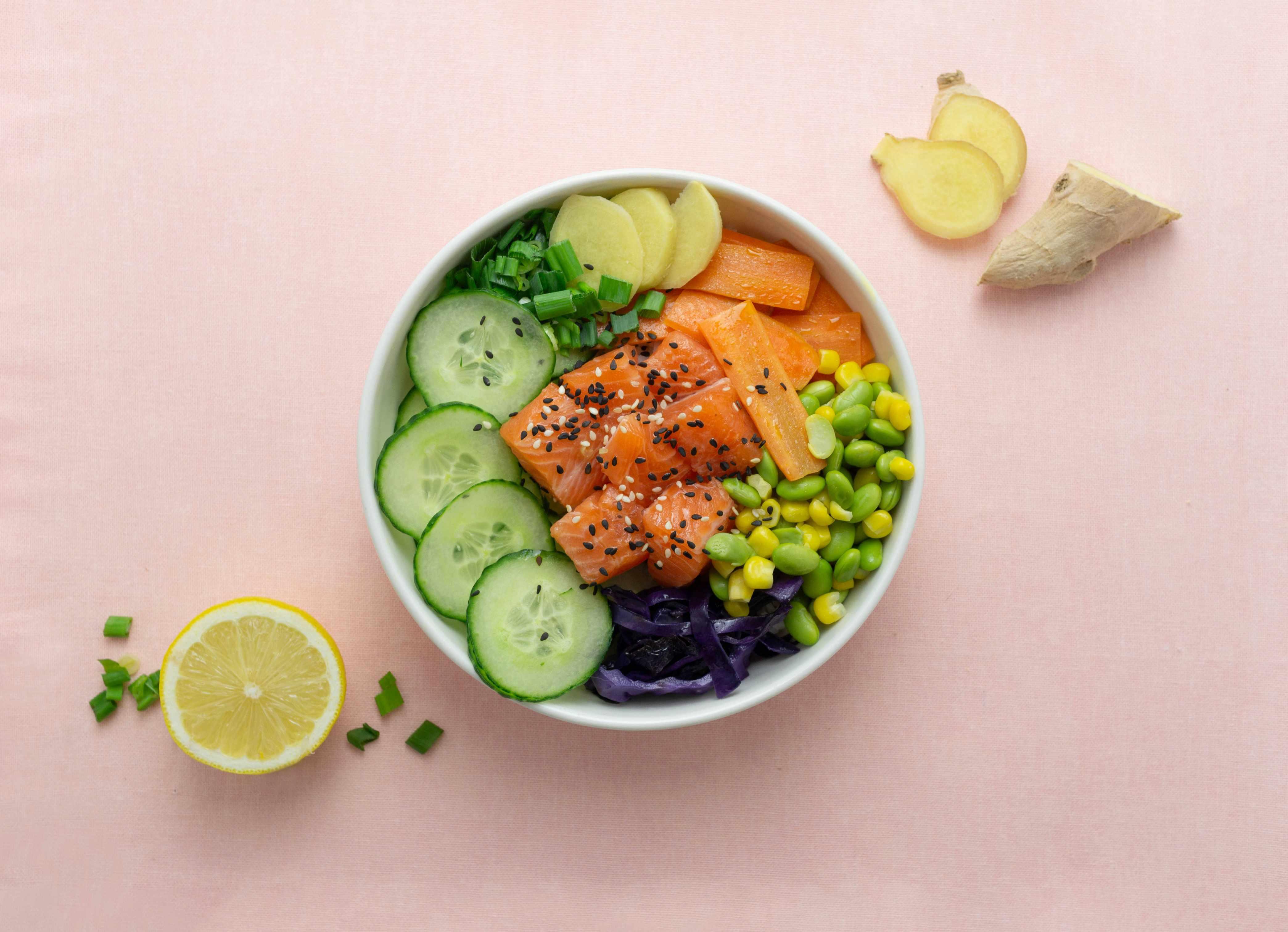 A generic poke bowl is pictured with various vegetables atop a pink background.