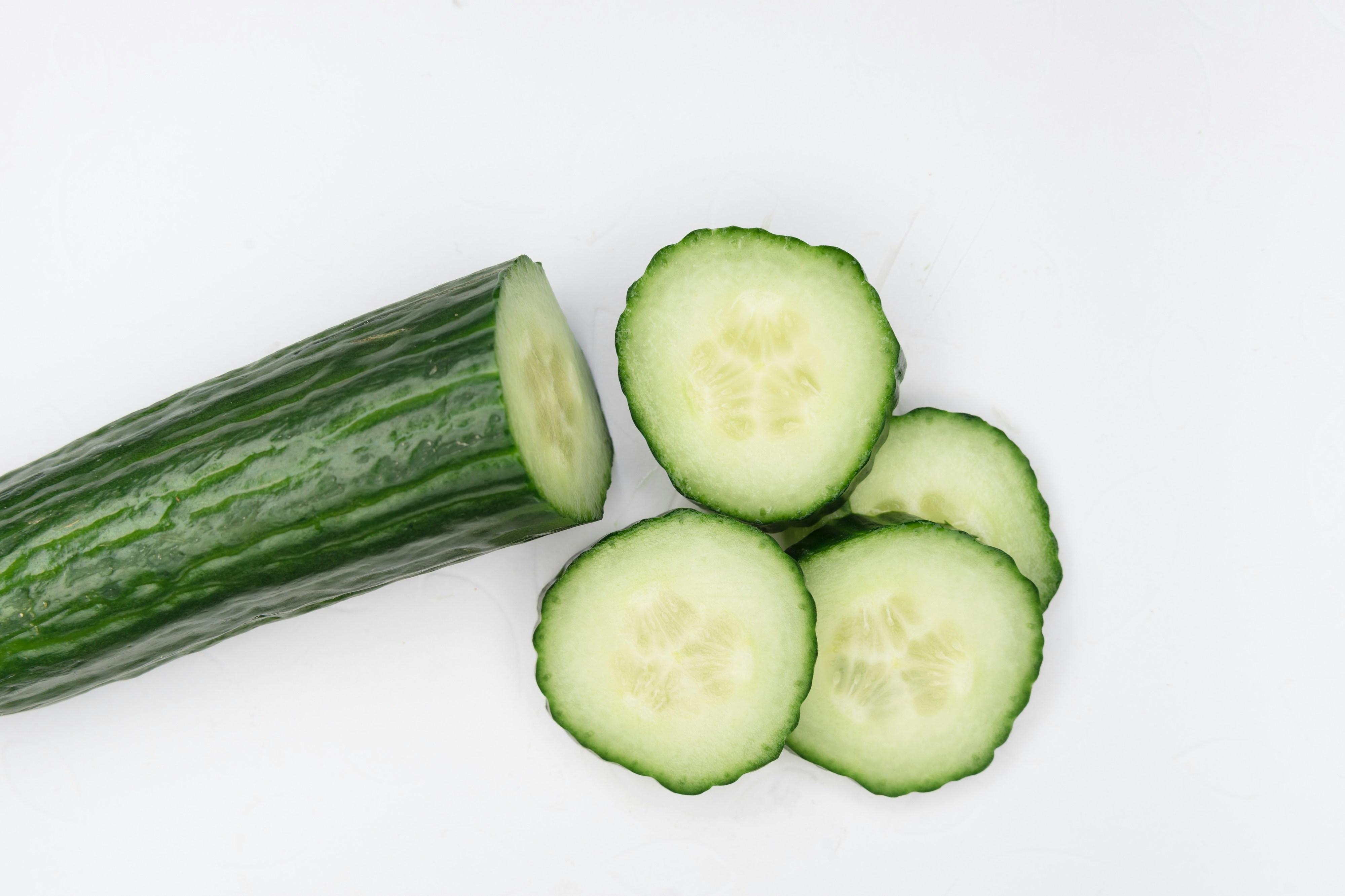 A chopped cucumber is pictured with four pieces sitting beside the rest of the cucumber.
