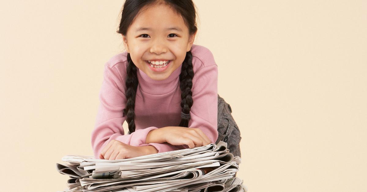 Young woman with braids sitting on top of a pile of newspaper. 