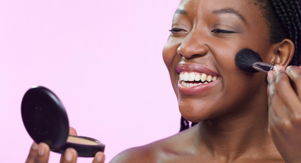 A woman applying face powder and smiling. 