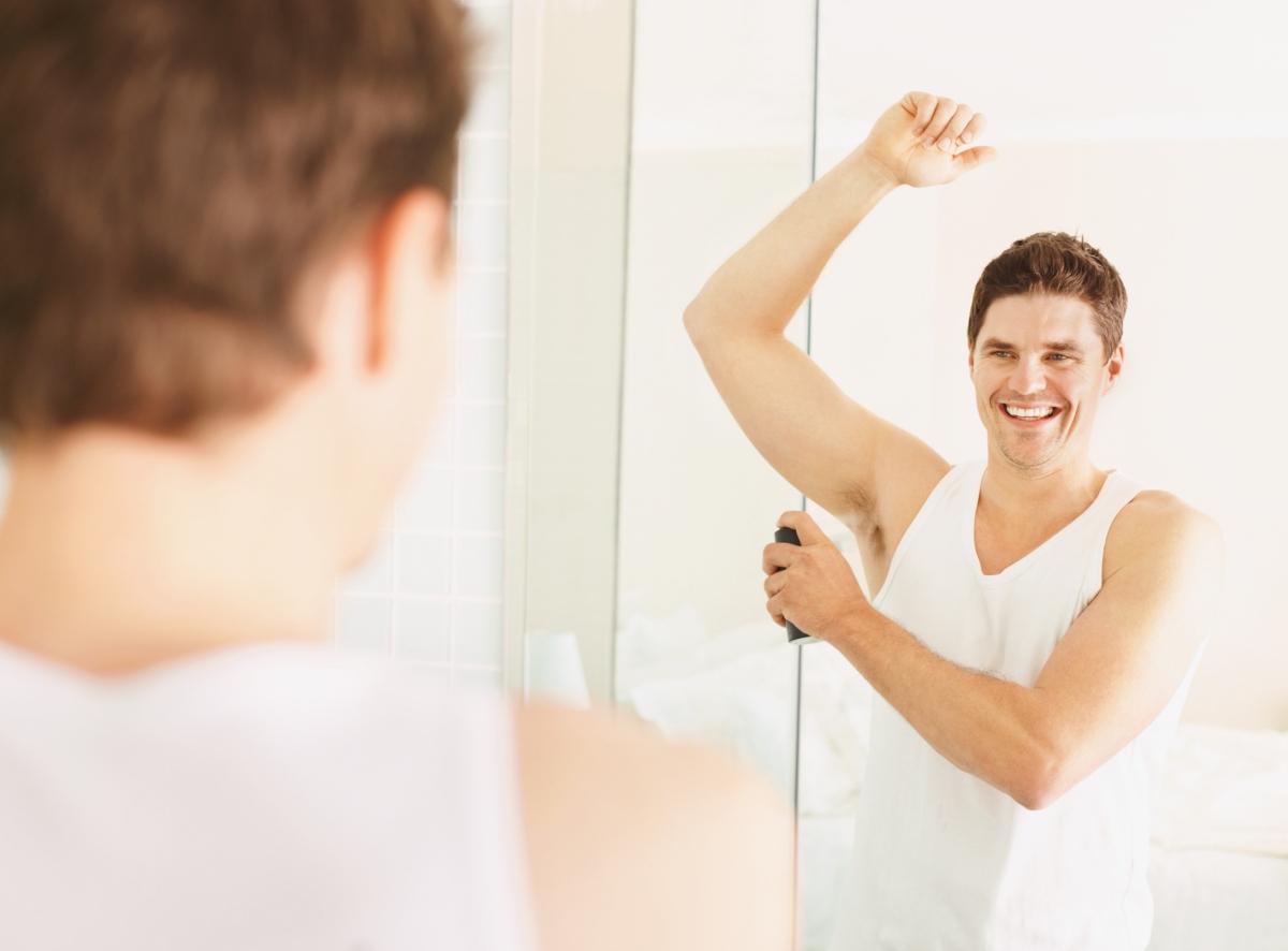 man in white tank spraying on deodorant