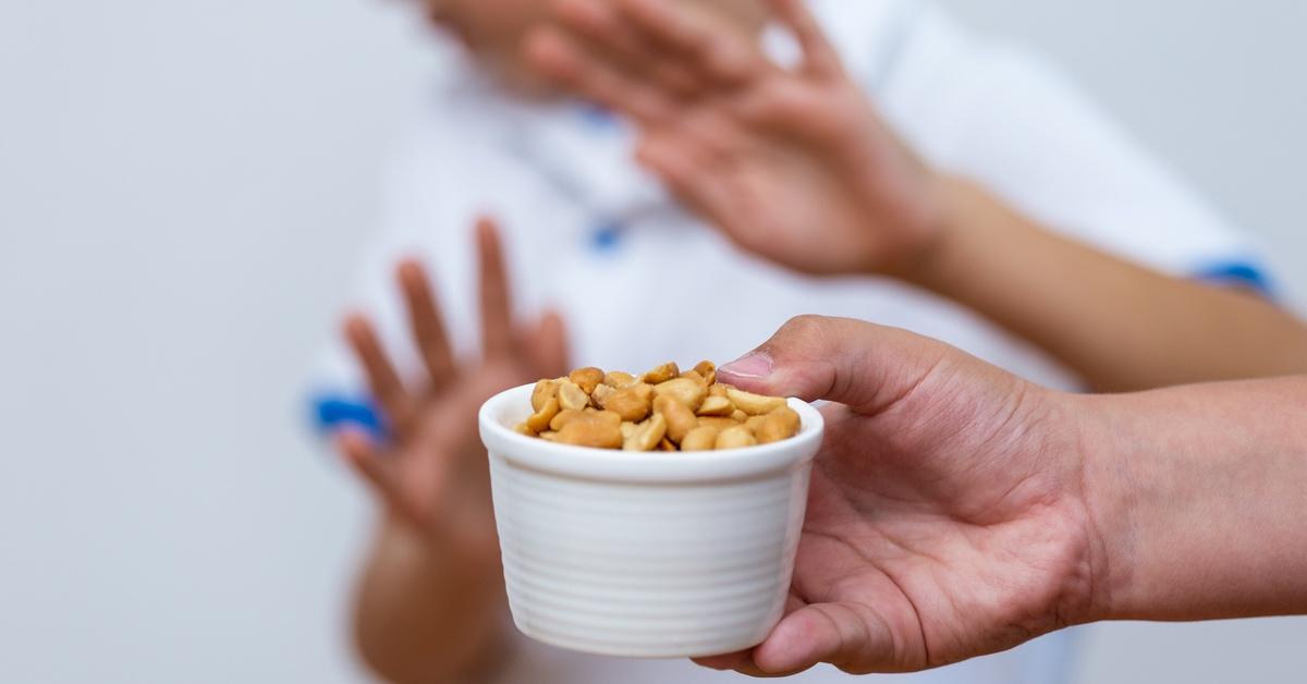 Person offering a bowl of peanuts to a child, who is holding up his hands to say no.