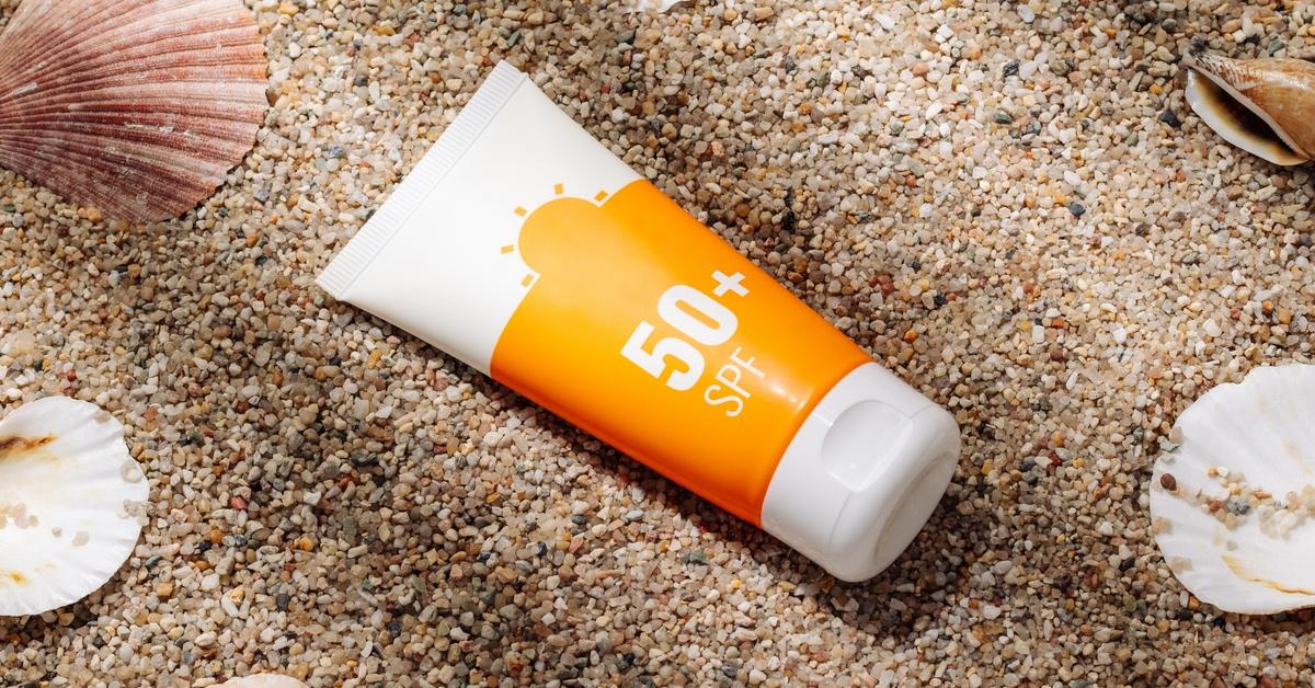 Sunscreen SPF 50 plus in a white and orange on a sandy beach with shells. 