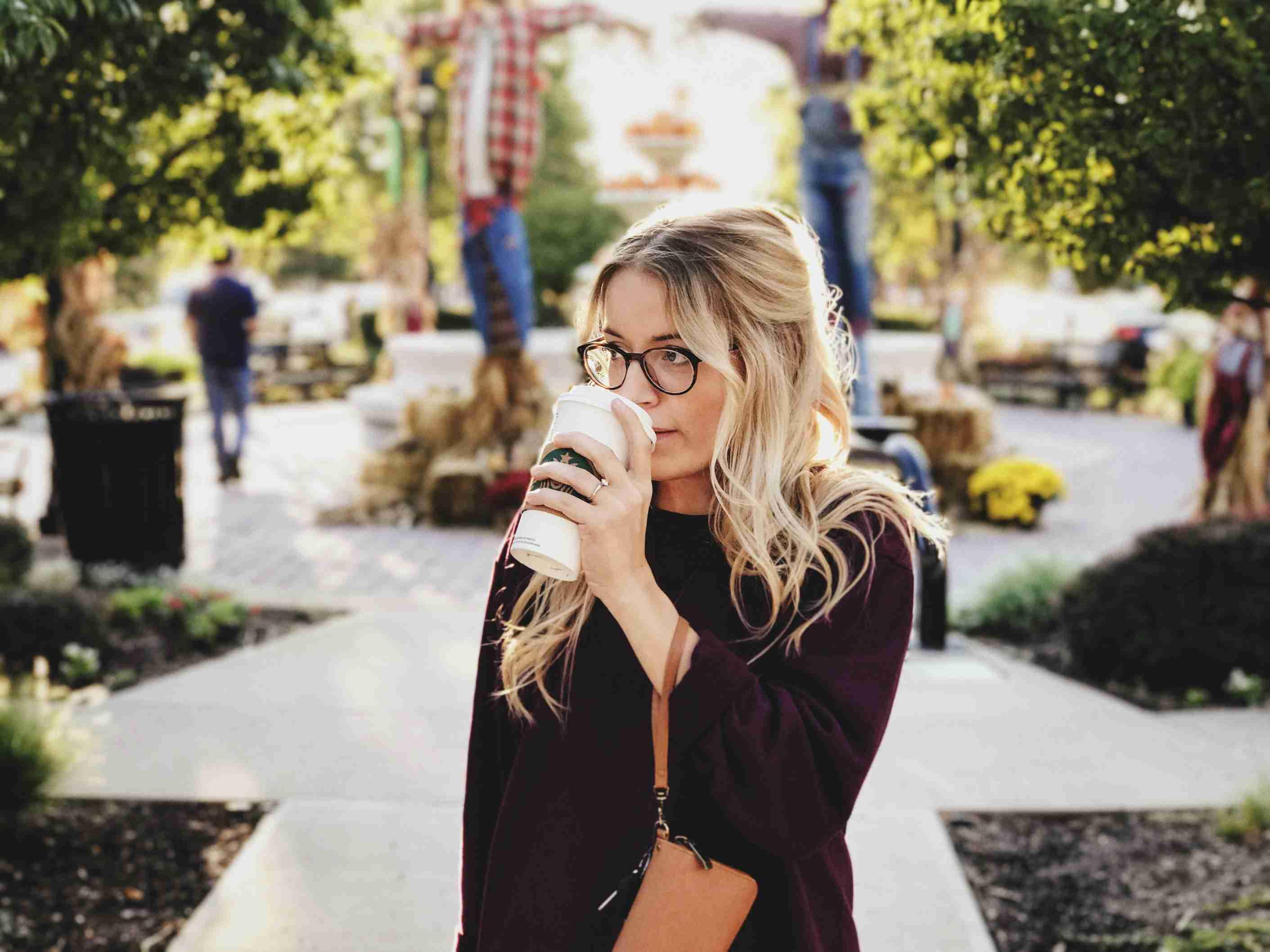 A teacher sips coffee from her cup while walking across a university campus.