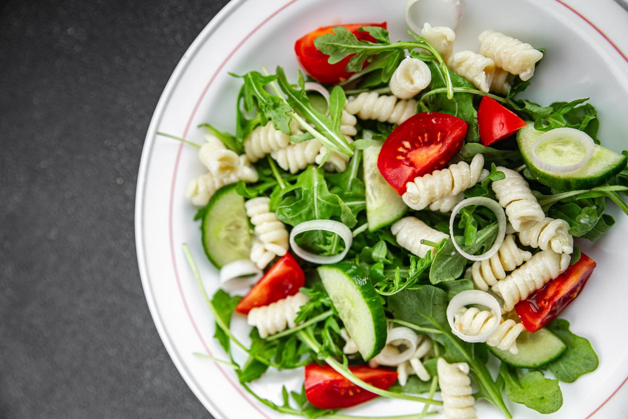 Close up view of a pasta salad with greens, cucumbers, and cherry tomatoes.