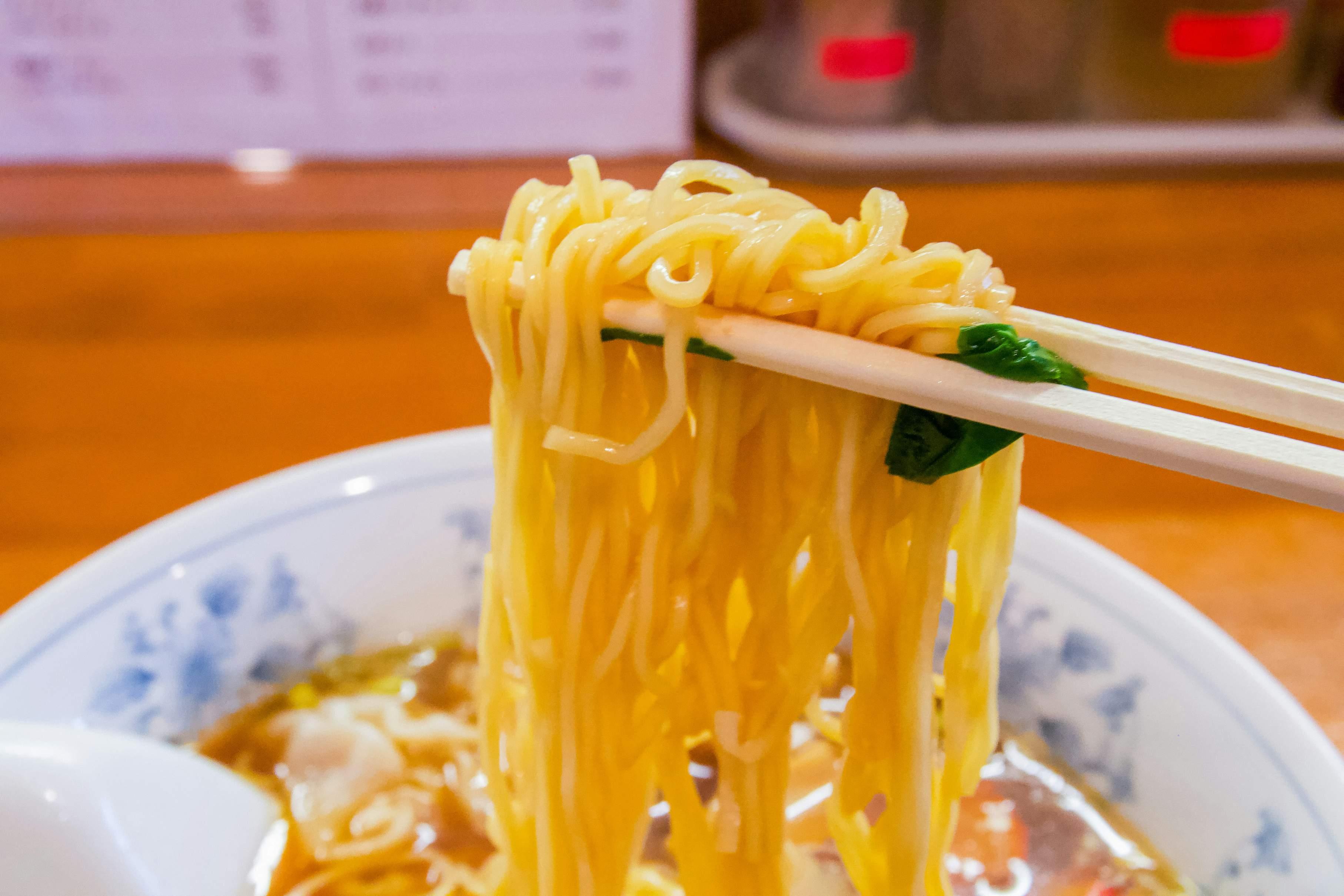 A bowl of ramen is pictured with noodles contained within two chopsticks.