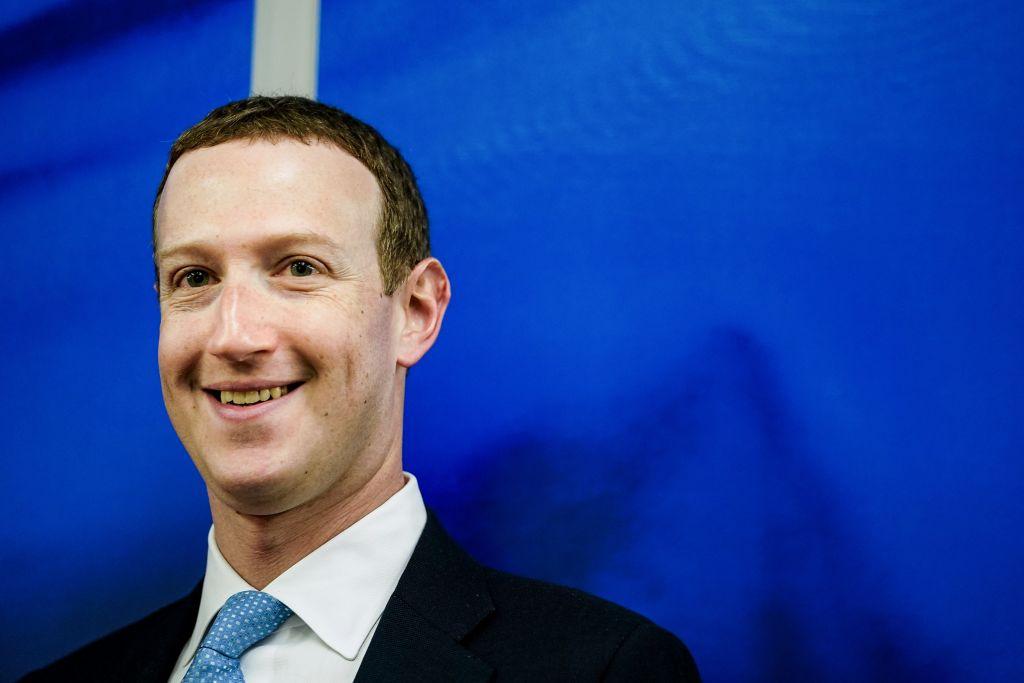 Mark Zuckerberg, seen here from the neck up, smiles against a blue backdrop.