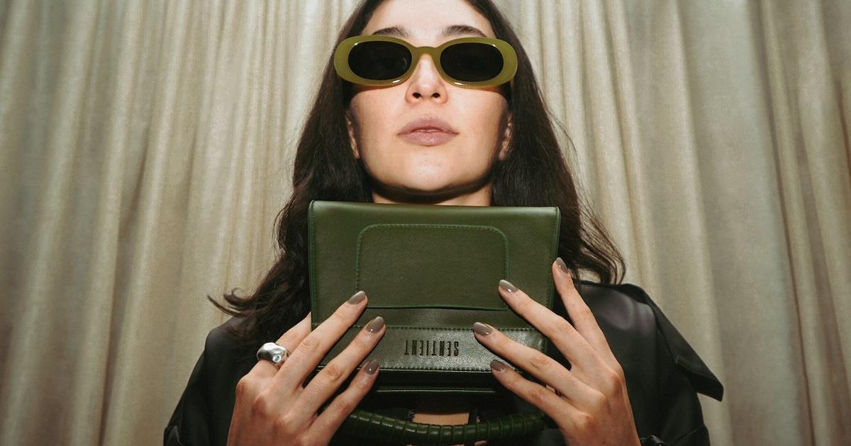 A woman wearing sunglasses holds a green purse