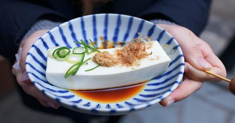 Pair of hands holds blue and white bowl with a block of tofu in sauce with seasonings