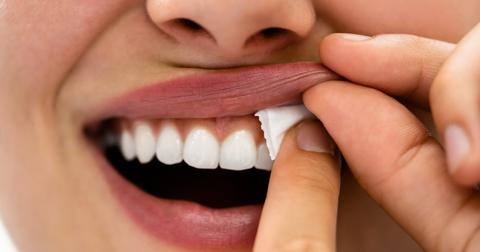 A close up of a woman putting a nicotine pouch in her mouth on her gums.