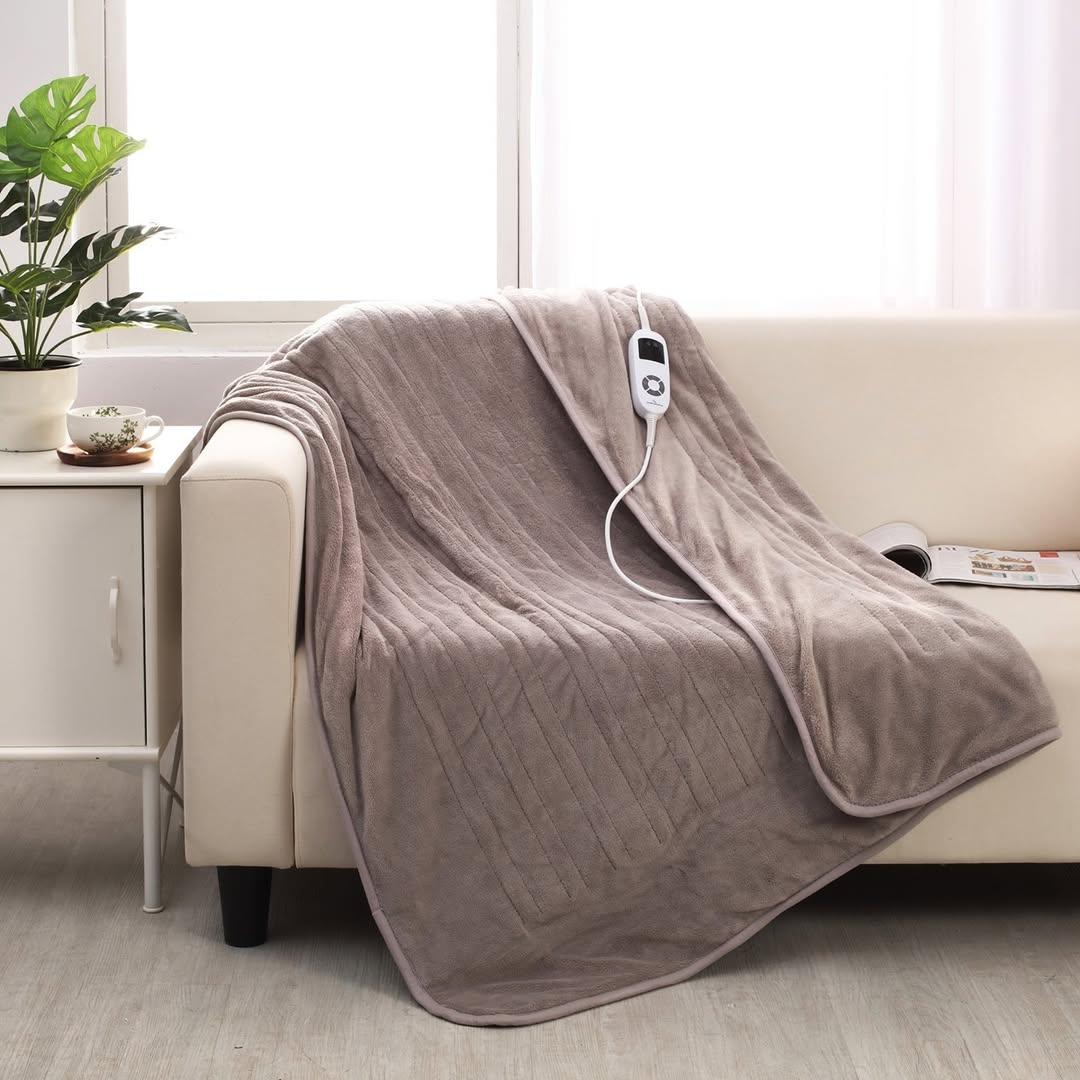 The gray "Daniel Brighton Electric Blanket"from the Catch Australia brand is pictured on a cream colored sofa.