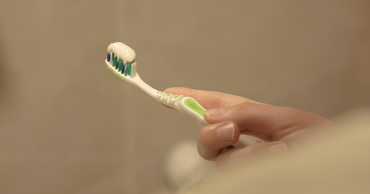 A person holds a green and white toothbrush after applying white toothpaste to the bristles 