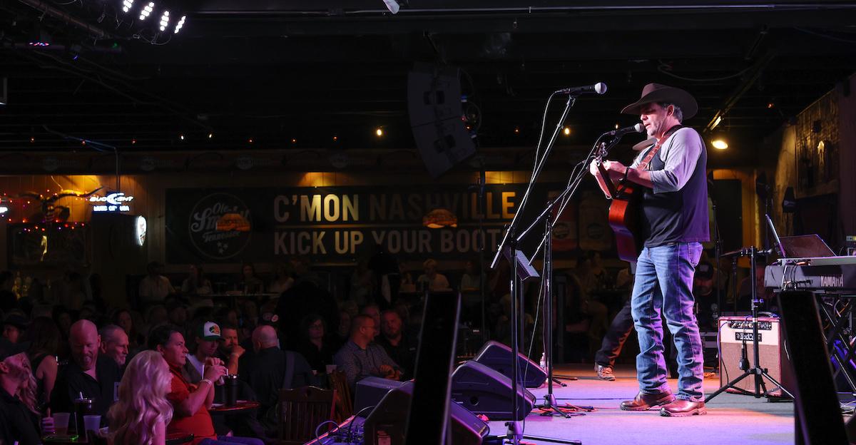 Man onstage with a guitar in front of a microphone performing a concert.