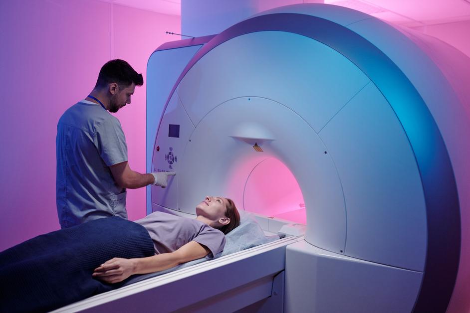 Young doctor pressing button on MRI machine as patient enters the machine.