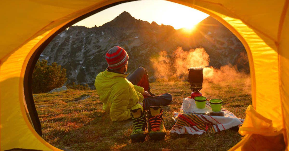 Campers beholding sunset outside the tent while boiling water (Representative Cover Image Source: Getty Images | Maya Karkalicheva)