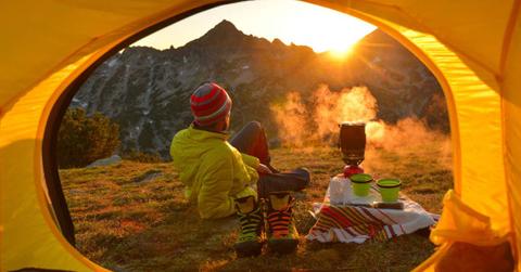 Campers beholding sunset outside the tent while boiling water (Representative Cover Image Source: Getty Images | Maya Karkalicheva)