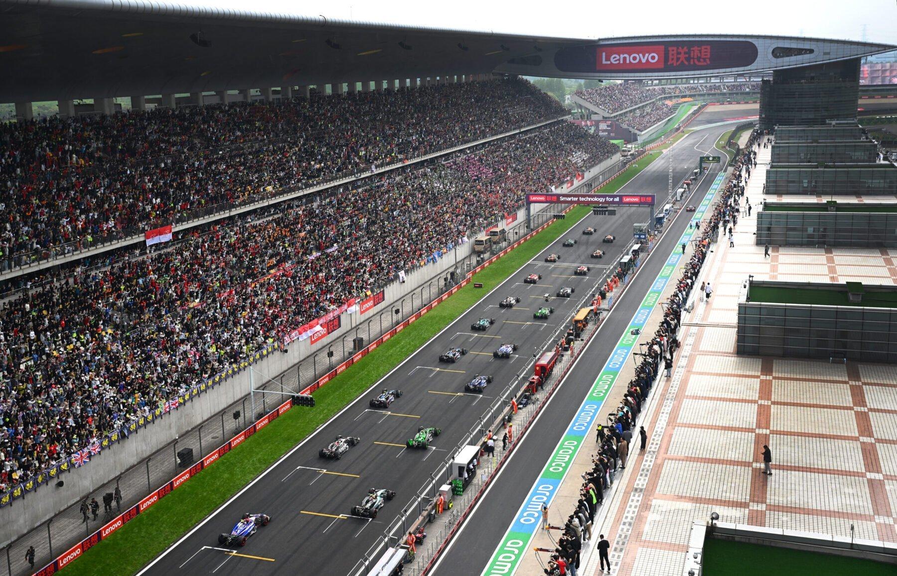 An F1 race located in China features a slew of cars on a track beside a large crowd.