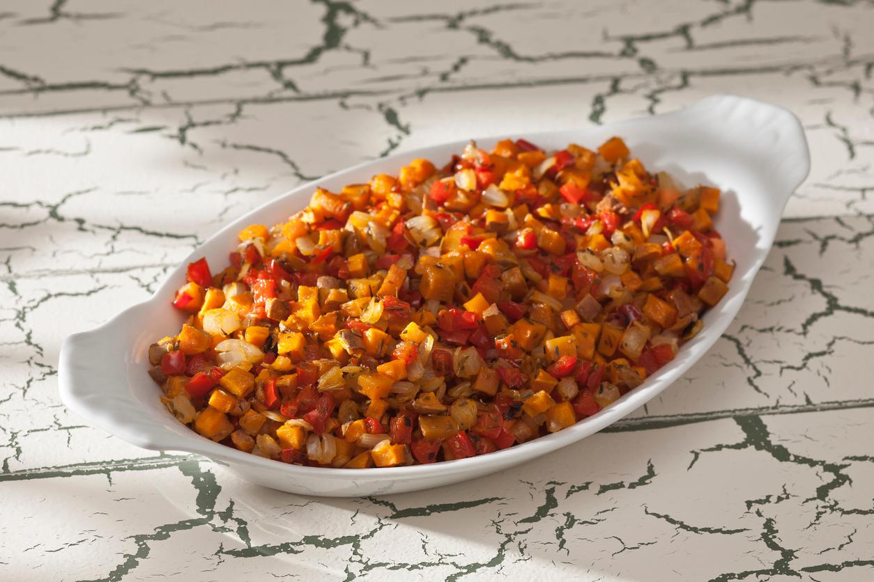 A sweet potato hash is pictured in a white bowl atop a marbled counter.