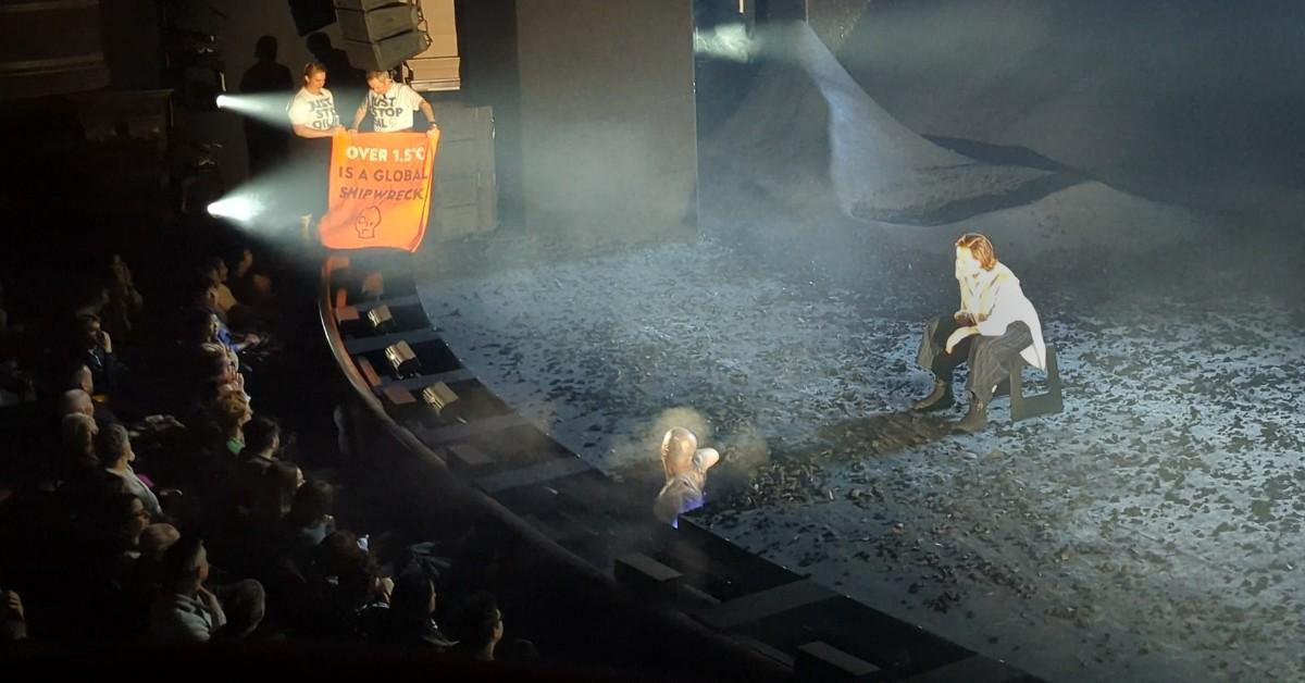 Protesters hold a sign that says "over 1.5C is a global shipwreck" in the middle of Sigourney Weaver's performance