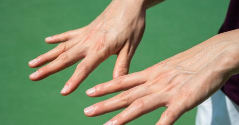 A person holds out their hands with prominent veins with a green background.