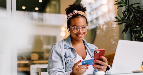 A woman smiles at her phone as she pays online with a credit card