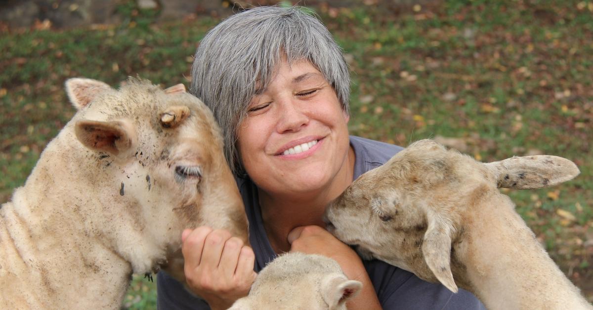 Smiling woman cuddles three goats