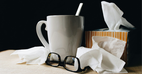 A coffee mug and tissues pile up next to a pair of glasses