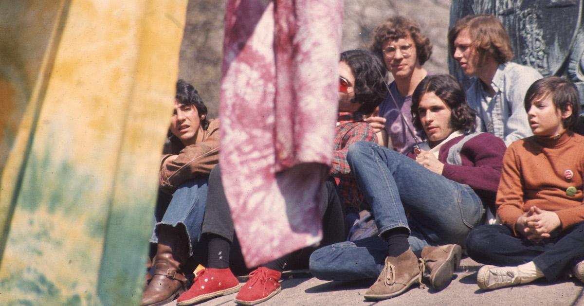 Six people sit in a park with tie-dyed tapestries.