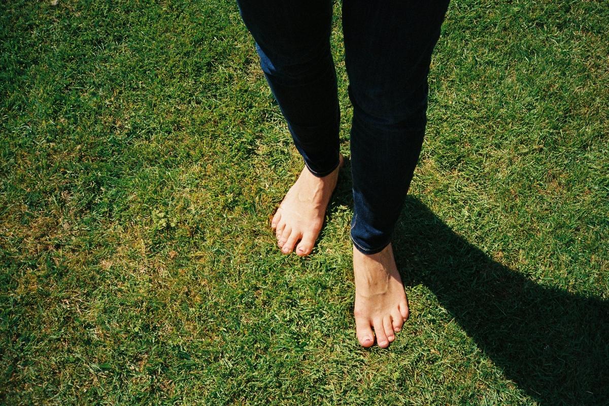 barefoot person in jeans stands on grass