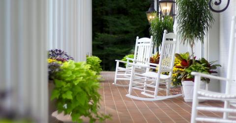 Variety of potted plants on a porch with white rocking chairs