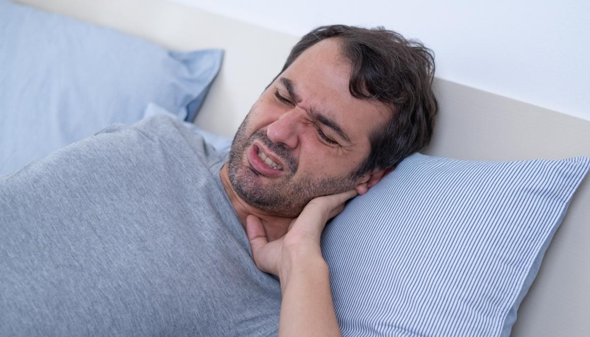 Man in bed grimacing with neck pain