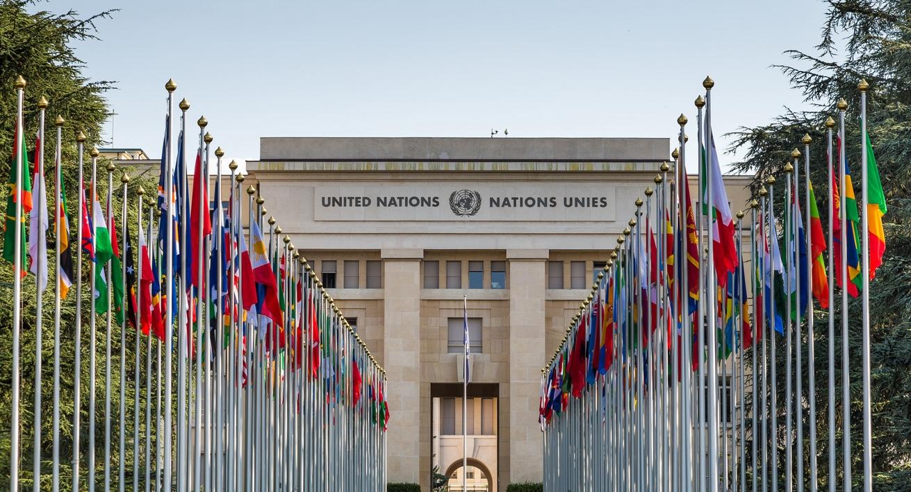 The exterior of the United Nations building lined with many flags and flagpoles, representing all the member nations of the UN, located in Geneva, Switzerland.