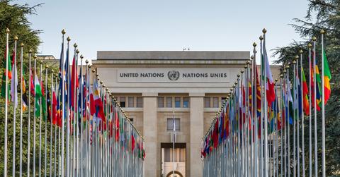 The exterior of the United Nations building lined with many flags and flagpoles, representing all the member nations of the UN, located in Geneva, Switzerland.