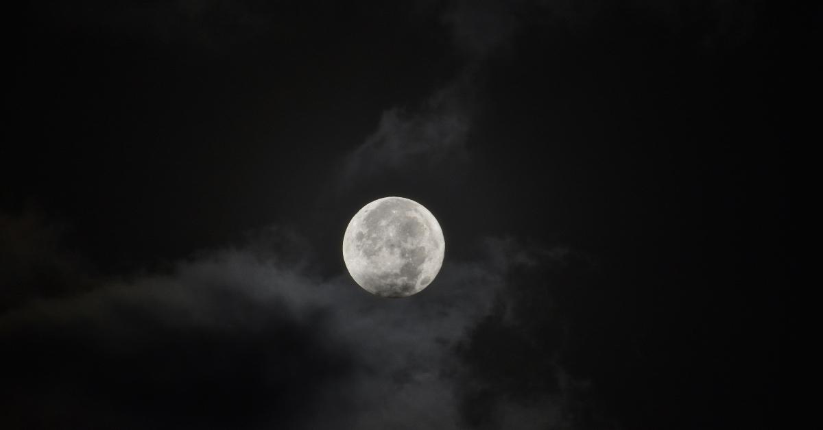 A full moon rises at night with clouds. 