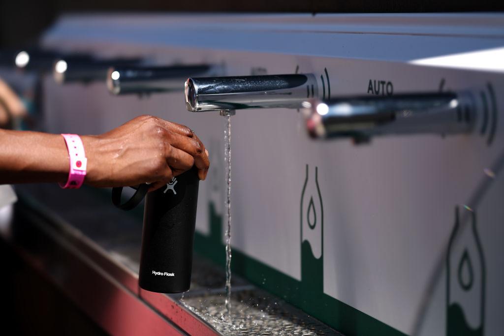 Wimbledon attendees refill their water bottles, including one attendee with a black HydroFlask bottle, at a public water refilling station.