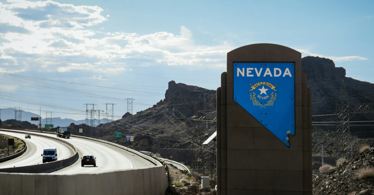 A sign for the state of Nevada stands next to a roadway outlined with power lines