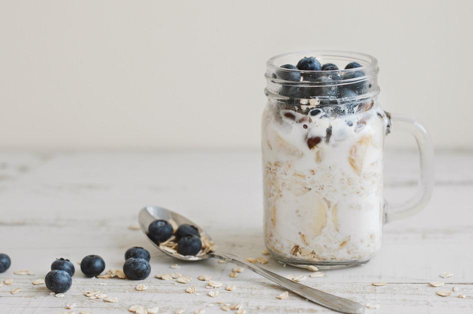 A jar of overnight oats with blueberries on top sits next to a spoon with blueberries on it. 