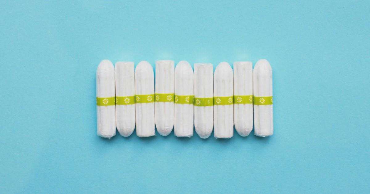 A row of white tampons with a green floral wrapper lay together on a blue background