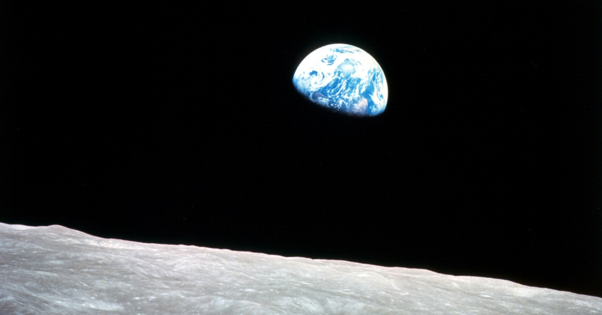 Earth appears from behind the moon, with just half of the planet visible in the black of space