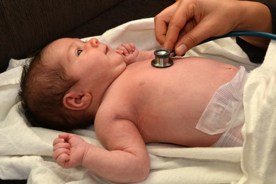 Newborn baby getting their heart beat checked by a doctor while lying on top of a white blanket. 