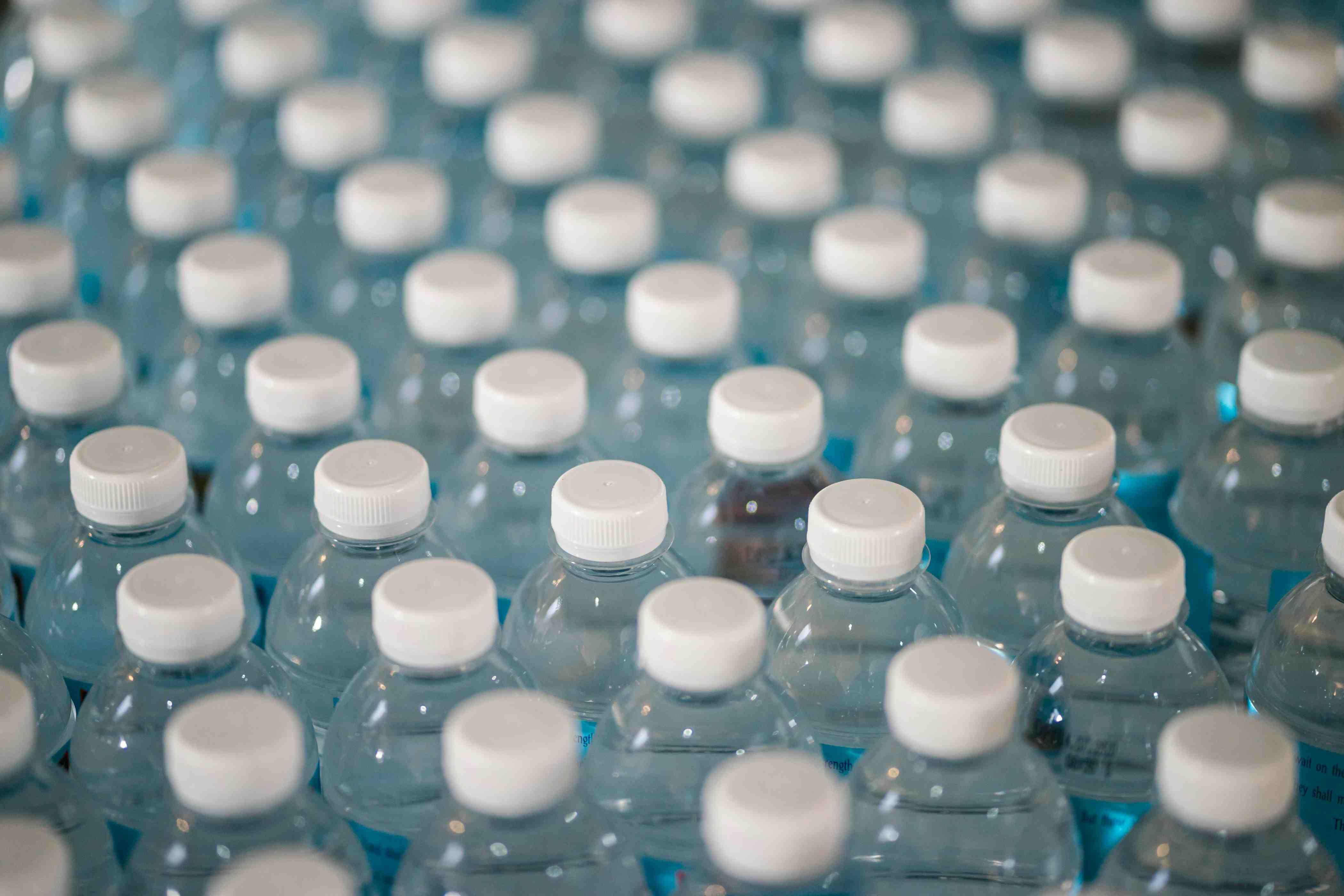 A group of dozens of water bottles are pictured standing beside one another.